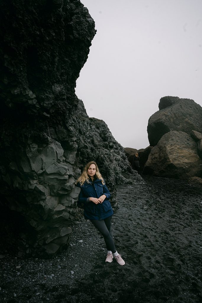 woman leaning on rocks in the black sand beach iceland