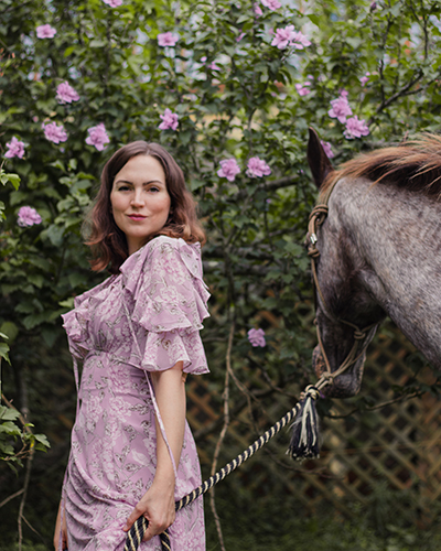 woman in pink standing in front of bush with pink flowers, holding a horse