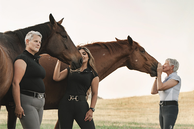 three women standing with two horses in a pasture